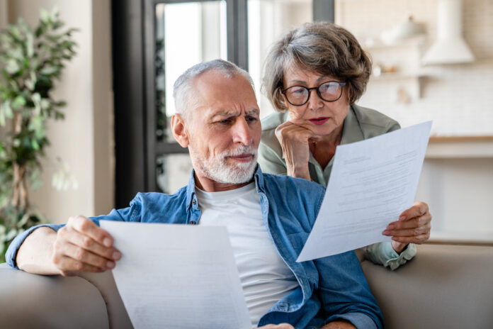 Senior old elderly spouses grandparents reading documents together at home.