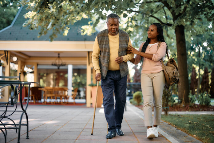 Smiling woman walking with her senior father while visiting him at nursing home.
