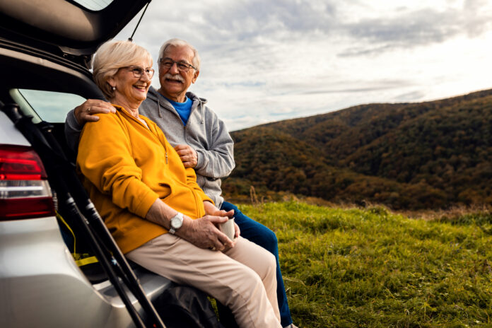 Senior couple sitting against the car, resting after hiking in countryside.