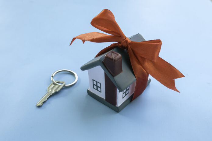 House Key with Miniature House Gift Wrapped with Red Ribbon on blue Surface