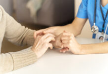 Early Alzheimer’s Detection: Would You Want to Know? Young woman's hands hold grandmother's hands, an elderly patient. Handshake, caring, trust and support. Medicine, family and healthcare.