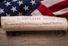 The First 250 Years: The Ideals That Founded America United States Declaration of Independence rolled in a scroll on a vintage American flag and rustic wooden board